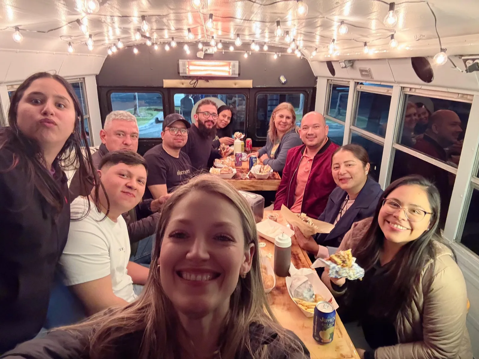 Clientes comiendo dentro del Latinus Gastrobus — un bus escolar pequeño transformado en un comedor rodante con luces cálidas y mesas